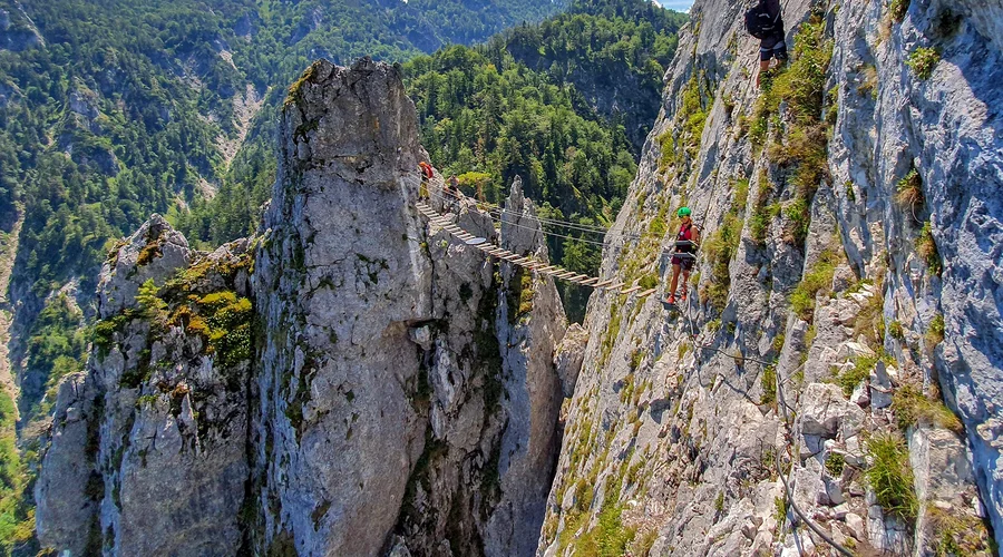 Kletterer am Drahtseil des Drachenwand-Klettersteigs bei Mondsee, im Hintergrund das Salzkammergut-Panorama
